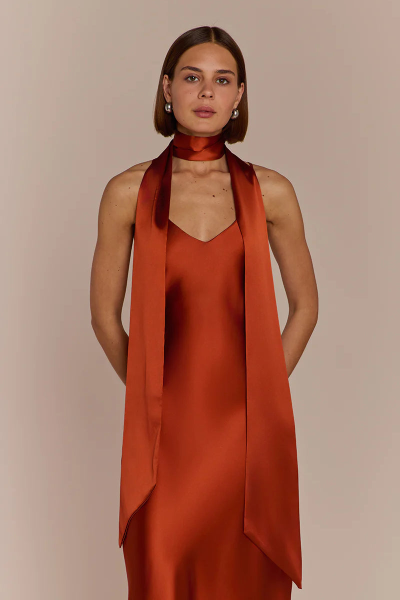 Woman wearing a rust-colored dress with a matching scarf against a beige background