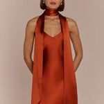 Woman wearing a rust-colored dress with a matching scarf against a beige background