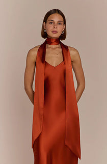 Woman wearing a rust-colored dress with a matching scarf against a beige background