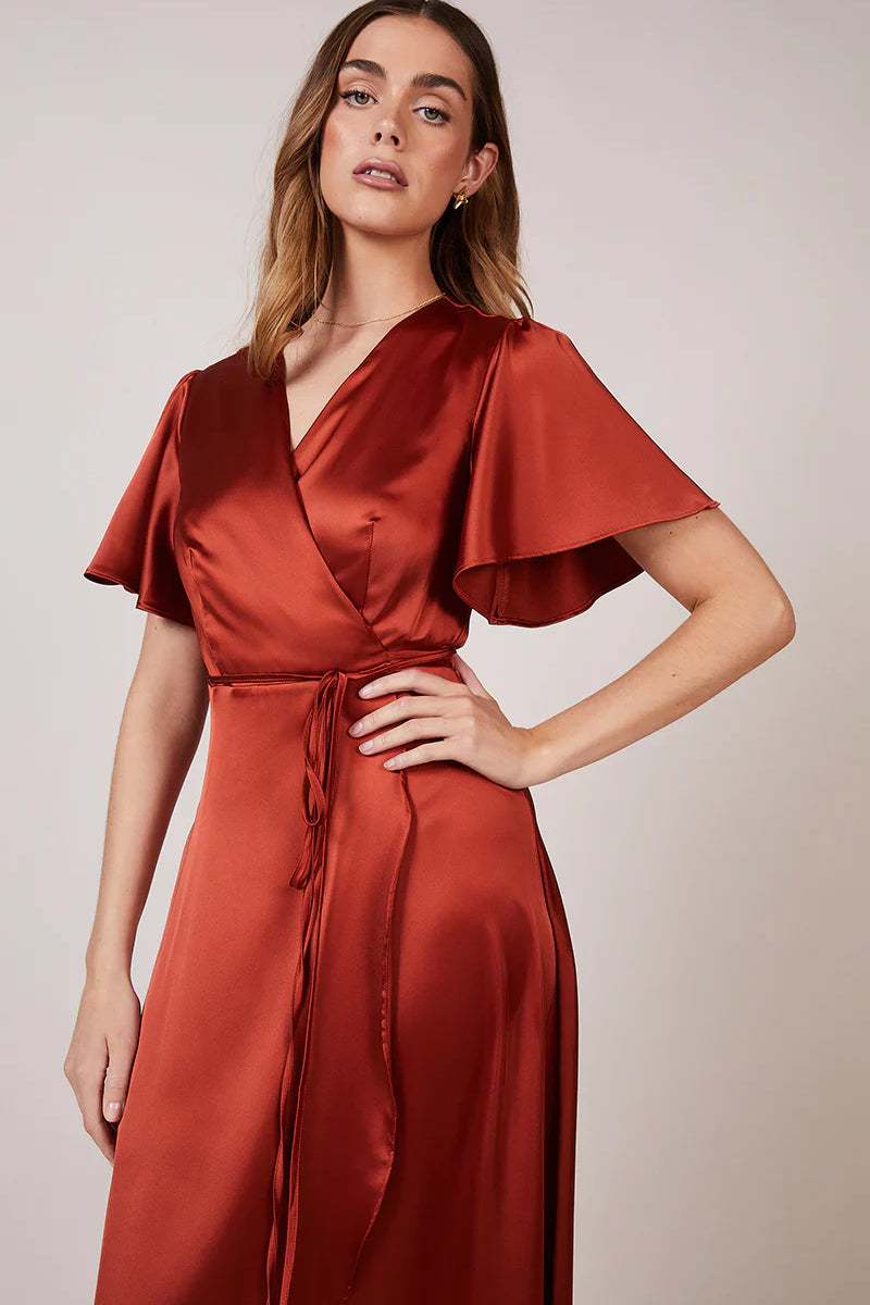 A woman wearing a burnt orange satin bridesmaid dress with a v-neck, short draped sleeves, and a waterfall hem.