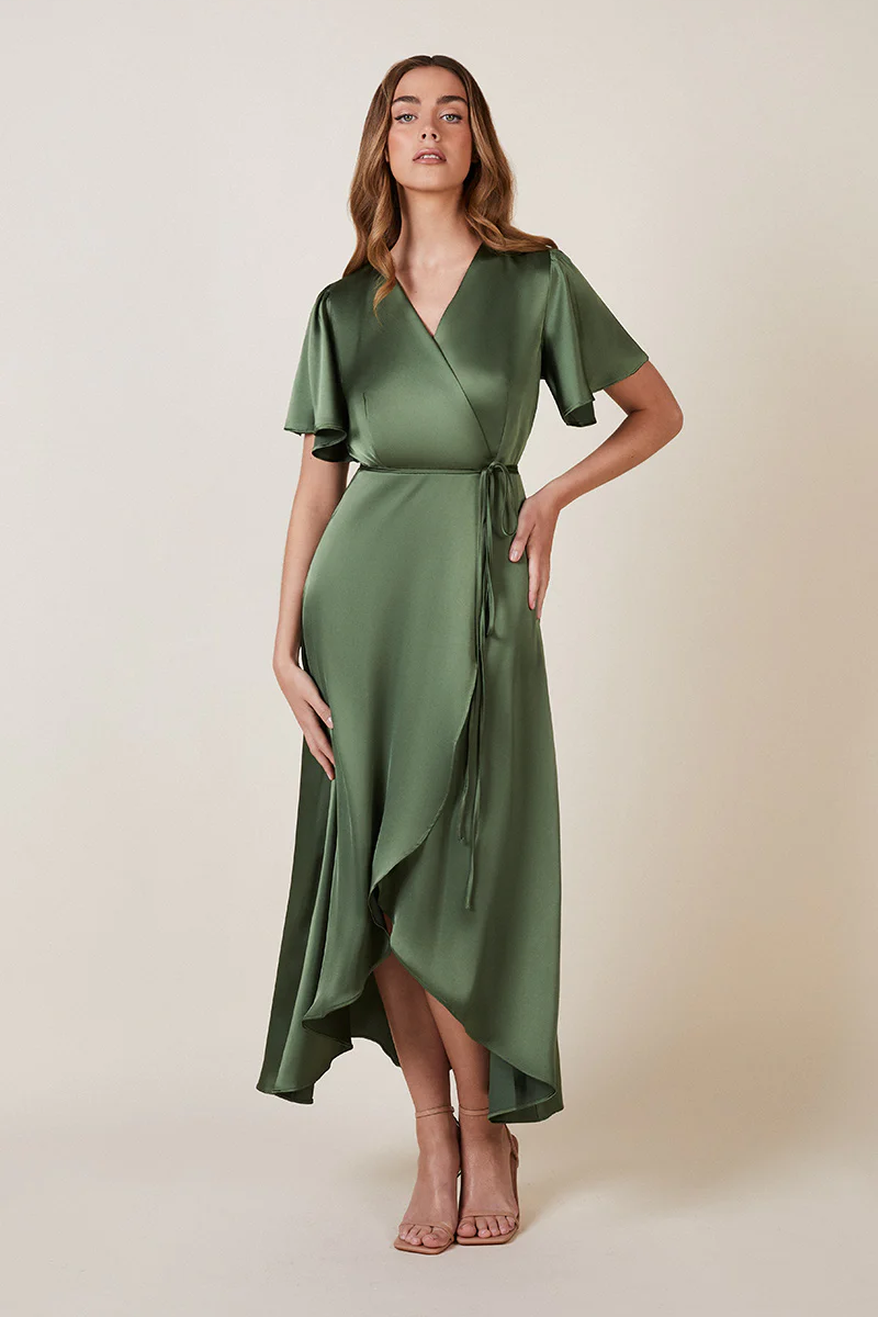 A woman standing and posing in an olive green, V-neck, short-sleeved, midi-length bridesmaid dress with a waterfall hem.