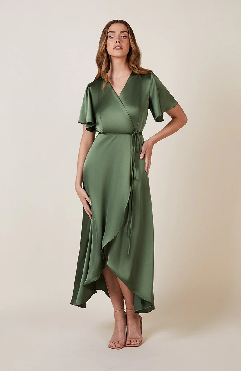 A woman standing and posing in an olive green, V-neck, short-sleeved, midi-length bridesmaid dress with a waterfall hem.