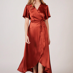 A woman wearing a burnt orange satin bridesmaid dress with a v-neck, short draped sleeves, and a waterfall hem.