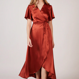 A woman wearing a burnt orange satin bridesmaid dress with a v-neck, short draped sleeves, and a waterfall hem.