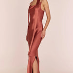 Woman wearing a rust-colored satin dress with a high slit on a beige background