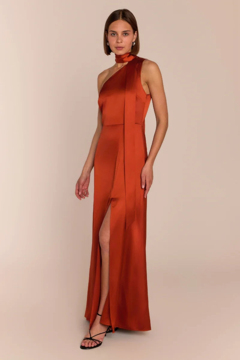 Woman wearing a rust-colored halter neck dress with a slit on a beige background