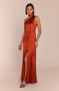 Woman wearing a rust-colored halter neck dress with a slit on a beige background