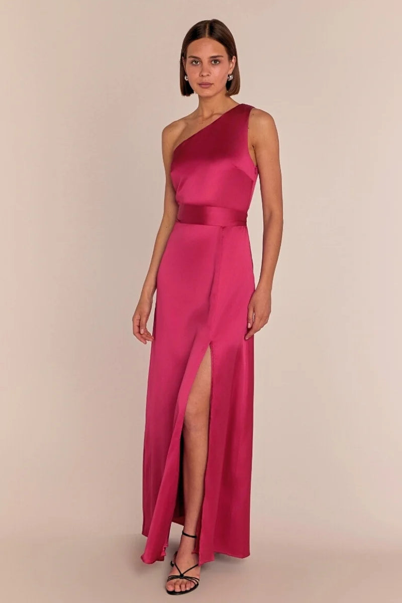 Woman wearing a pink one-shoulder gown with a slit on a beige background