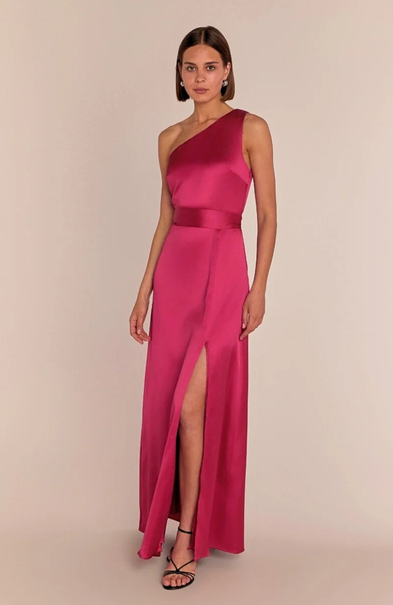 Woman wearing a pink one-shoulder gown with a slit on a beige background