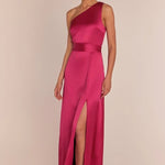 Woman wearing a pink one-shoulder gown with a slit on a beige background