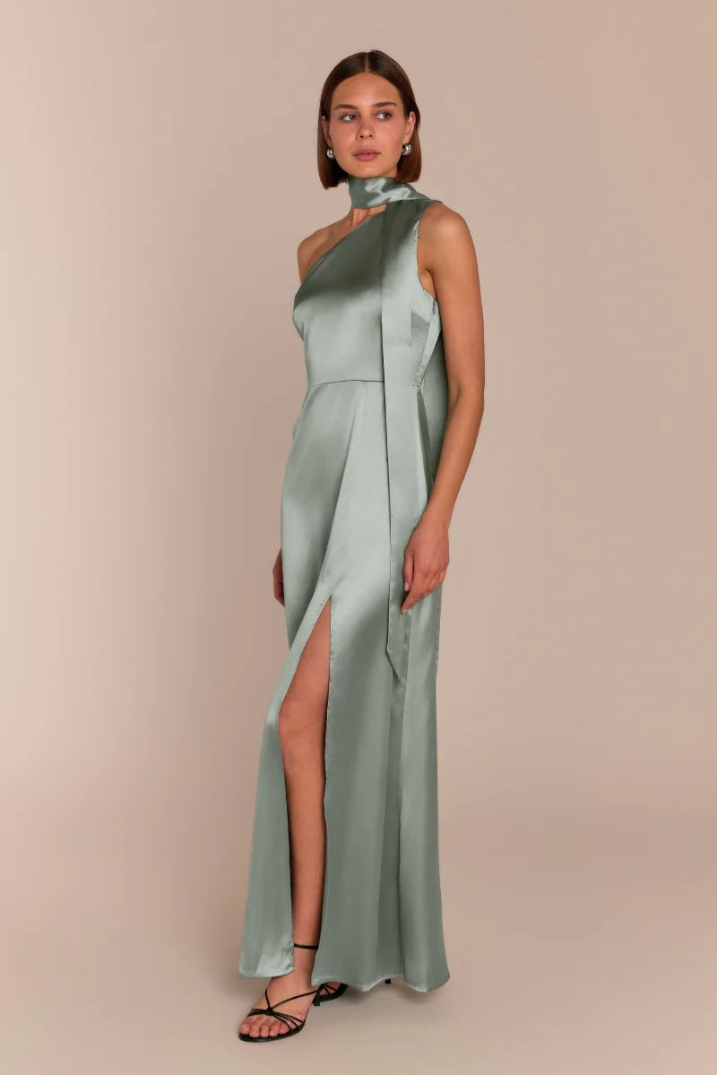 Woman wearing a light green one-shoulder dress with a slit on a beige background