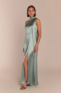 Woman wearing a light green one-shoulder dress with a slit on a beige background