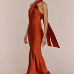 Woman wearing a rust-colored one-shoulder gown on a beige background