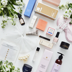 An assortment of luxury beauty products from The Ultimate Bridal Beauty Box, including skincare, cosmetics, and accessories displayed on a white surface with floral decorations.