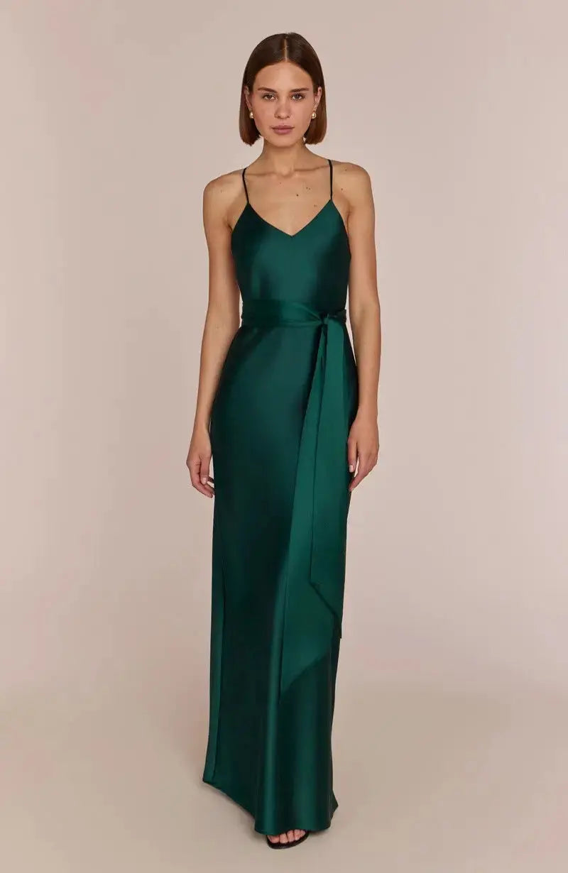 Woman wearing a Brooklyn strappy slip satin bridesmaids occasion-dress dark forest green against a beige background