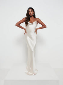 A woman wearing a maxi bridesmaid dress with a cowl neckline and spaghetti straps, in a champagne color.
